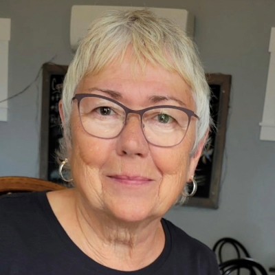 A woman in glasses sits outside a home. 